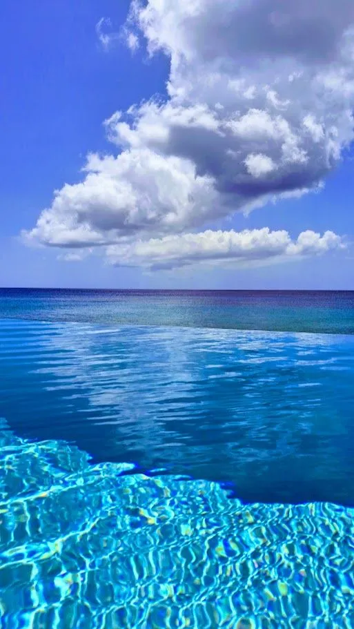 Bright blue pool and ocean under a towering tropical cloud